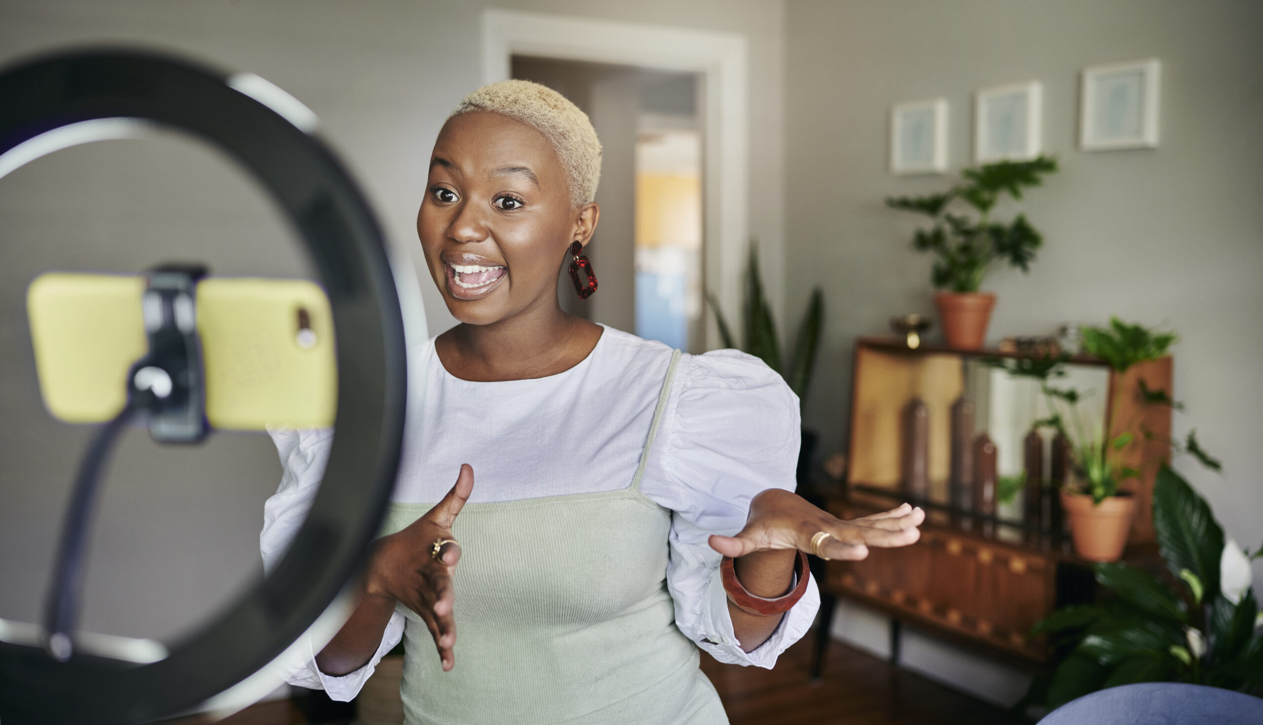 Smiling young African female influencer standing in her living room at home and talking during a vlog post using a smart phone